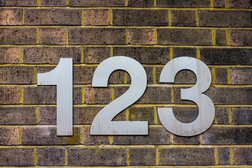 House number 123 with the one hundred and twenty three in large silver numbers on a yellow brick wall