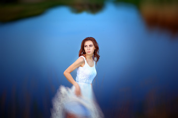 Fototapeta na wymiar beautiful woman with brunette hair in white dress with frame in hand posing on a background of lake