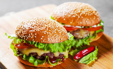 two burger with meat, cheese and vegetables on wooden board