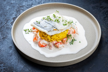 Fried haddock filet with saffron rice and shell prawns in crab sauce as closeup on a modern design plate
