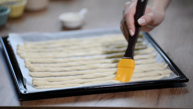 Woman in kitchen brush grissini with olive oil. Cooking Italian grissini.
