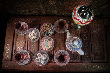 Arabian tea in glass with eastern snacks on vintage wooden surface. Eastern tea concept. Low light lounge interior with carpet. Empty space.