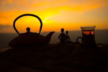 Arabic tea in traditional glass and pot on desert at sunset. Eastern tea concept. Artwork decoration on sand with tea.