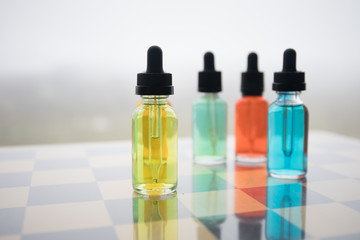 Vape concept. Beautiful colorful vape liquid glass bottles outdoor on stones. Useful as background or electronic cigarette advertisement.