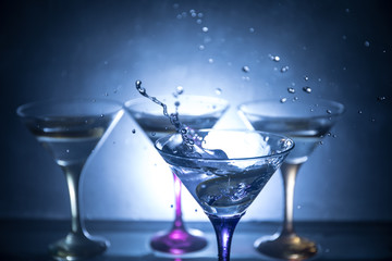 Martini cocktail glass in hand splashing on dark toned smoky background or colorful cocktail in glass with splashes and olives. Party club entertainment. Mixed light. Selective focus