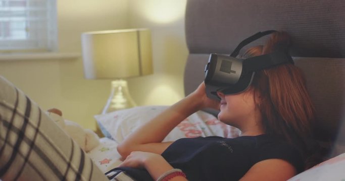 Laying down on the bed teenager girl she using a virtual reality glasses to exploring the new invention of a VR , she are very impressed