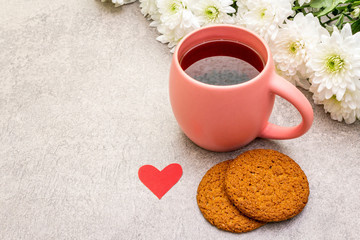 Romantic breakfast concept. A cup of black tea, oatmeal cookies, bouquet of chrysanthemums. For Valentine's Day or March 8, on a stone background