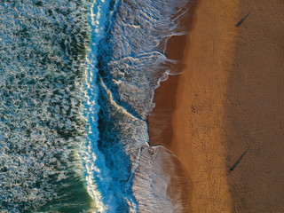 Fototapeta na wymiar Aerial view from a sandy beach with people walking at the sunset. Drone photo
