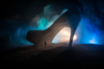 Artwork decoration. Silhouette of a man standing in the middle of the road on a misty night with giant high heel women shoes. Women power or women domination concept.