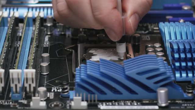 Build a computer, close-up view, 4K. A male service worker applies a layer of thermal paste to the CPU.