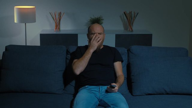 tired and sleepy man on the sofa watching tv yawning and falling asleep