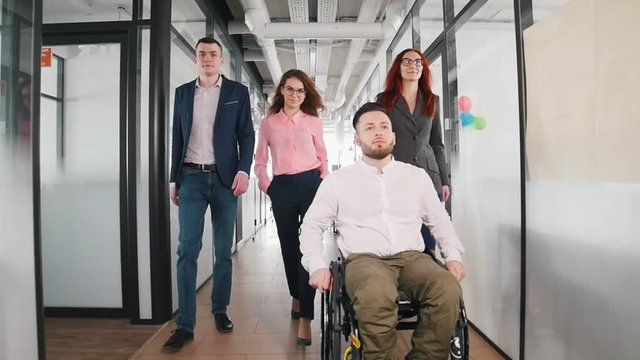 A successful business people walking through the corridor. A man in a wheelchair going first