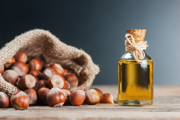 Hazelnuts, filbert in burlap sack and hazelnut oil in glass of bottle on wooden backdrop. heap or...
