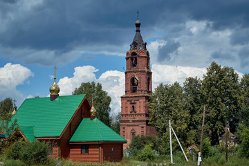 Old abandoned bell tower against the blue sky. In the foreground is a new Christian Orthodox Church with Golden domes. The bell tower is built of red brick. Church in rural or rural areas.