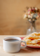 Food and dessert. Crackled crispy cookies with sugar on a plate and a cup of coffee on a wooden table. Blurry background with bouquet of flowers in a vase. Copy space.
