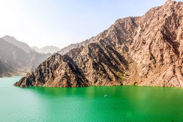 Obraz premium Emerald Green Mountain Lake Surrounded by Rocky Cliffs and Rugged Peaks