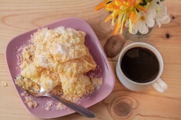 Dessert. Crackled crispy cookies with sugar on a plate and a cup of coffee on a rustic table. Blurry background with bouquet of flowers in a vase. Top view.