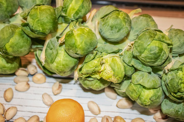 Healthy food - Close-up of part of a brussels sprout stalk laying on a white plank with an orange and pistachio nuts - selective focus