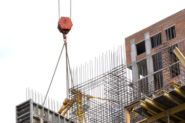 hook of a construction crane with cables and slings over the armature of an apartment building...