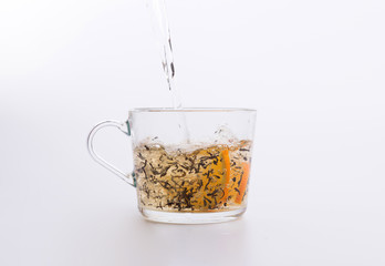 Water pouring into glass cup with tea and slices of orange isolated on white