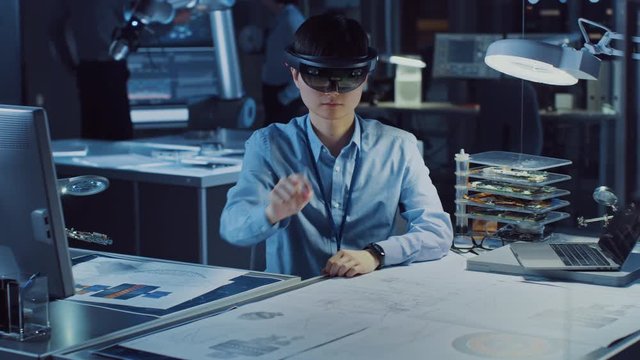 Professional Japanese Development Engineer is Working in a AR Headset, Moving Virtual Pieces Around and Looking at Graphics in the High Tech Research Laboratory with Modern Computer Equipment.