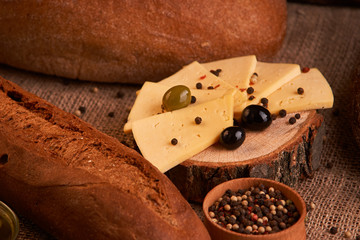 Traditional Dutch semi hard cheese served with olives on rural table with sacking. With baguette and bread
