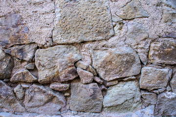 A texture of an old grey stone wall with concrete and big and small stones