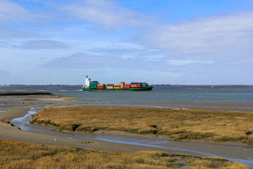 Fototapeta premium a ship sails along the salt marsh towards antwerp in springtime with a blue sky