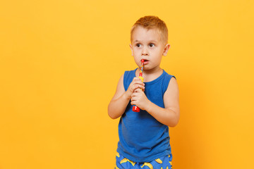 Kid boy 3-4 years old in blue shirt brush his teeth with toothbrush isolated on bright yellow orange wall background, children studio portrait. People, childhood lifestyle concept. Mock up copy space.