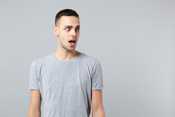 Obraz premium Portrait of shocked young man in casual clothes standing looking aside, keeping mouth open isolated on grey wall background in studio. People sincere emotions, lifestyle concept. Mock up copy space.