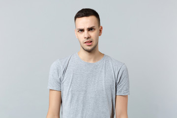 Fototapeta premium Portrait of perplexed concerned young man in casual clothes standing and looking camera isolated on grey wall background in studio. People sincere emotions, lifestyle concept. Mock up copy space.