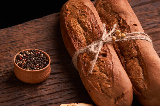Peppercorns in a wooden bowl on table with stack of bread and two baguettes. Homemade food