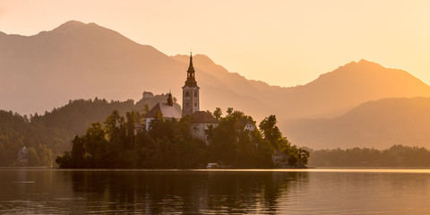 Fototapeta na wymiar Island with church in lake Bled on orange hazy morning