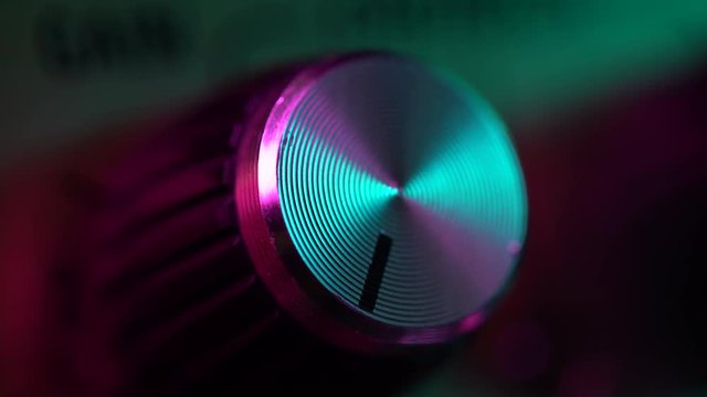 View of the control panel on a guitar amplifier. Tumblers, knobs and buttons. Male hand turn on and increasing music volume on amp. Colorful neon light. Macro view.