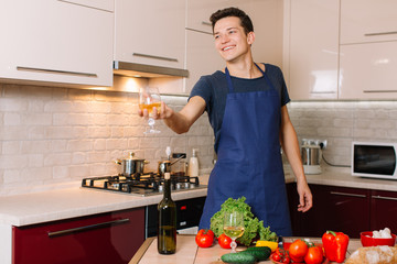 Handsome happy man is cooking and tasting wine on kitchen