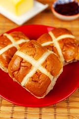 Three fresh hot cross buns on a red plate