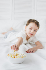 Obraz na płótnie Canvas Boy eating popcorn sitting in bed