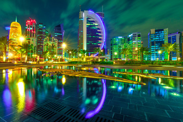 Doha West Bay high rises illuminated by night reflecting in downtown park. Colorful glassed skyscrapers of Doha skyline, Qatar, Middle East, Arabian Peninsula in Persian Gulf. Night urban scene.