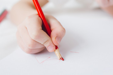 Boy draws with colorful pencils sitting on the bed