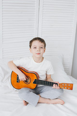 Boy playing a small guitar sitting on the bed