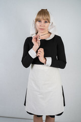 praying caucasian nun stands in a black dress and a white apostolic cap with a cross and an innocent face expression on white studio solid background