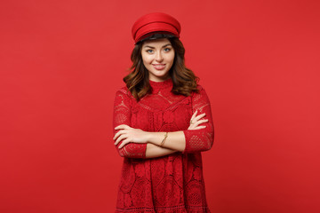 Naklejka premium Portrait of smiling young woman in lace dress and cap looking camera, holding hands folded isolated on bright red background in studio. People sincere emotions, lifestyle concept. Mock up copy space.