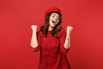 Obraz na płótnie Canvas Portrait of cheerful happy young woman in lace dress, cap clenching fists like winner isolated on bright red wall background in studio. People sincere emotions, lifestyle concept. Mock up copy space.