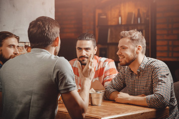 Guy with his back tells cool story. Rest of men sitting at table in beer bar listening to him carefully.