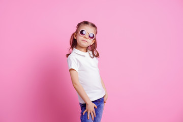Portrait of beautiful smiling cute model in trendy round sunglasses. Casual 7 y.o. girl posing isolated on pink background.