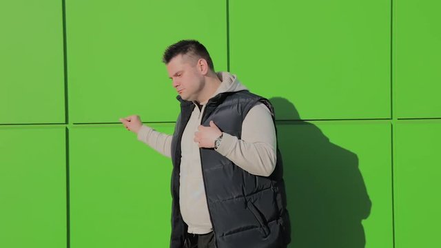 Fat man posing against a green wall near the store.