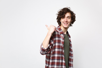 Portrait of cheerful young man in casual clothes looking camera, pointing thumb aside behind his back isolated on white wall background. People sincere emotions, lifestyle concept. Mock up copy space.