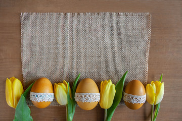 Wielkanocne tło - żółte pisanki i żółte tulipany na tkaninie z juty