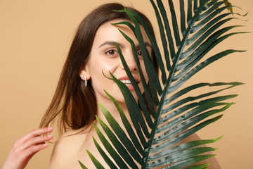 Naklejka premium Close up brunette half naked woman 20s with perfect skin, nude make up palm leaf isolated on beige pastel wall background, studio portrait. Health care cosmetic procedures concept. Mock up copy space.