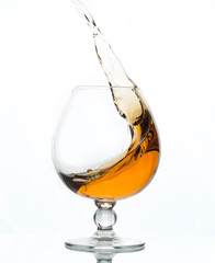 splash of brown cognac in transparent glass with reflection isolated on white 